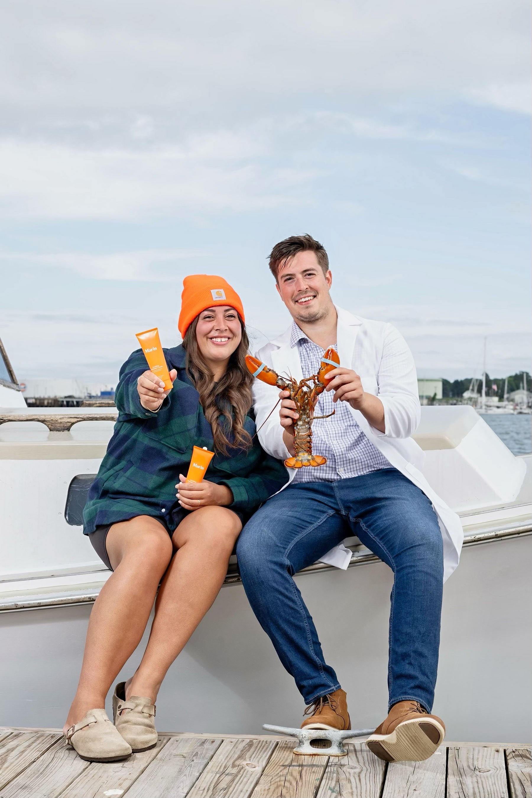 Two smiling people on a dock holding orange Marin tubes and a live lobster
